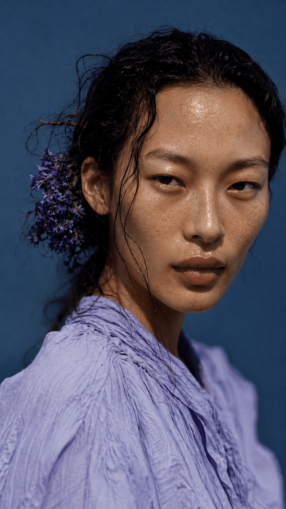 Editorial portrait of a woman with wet hair and freckles against a deep blue wall — a GPT Image generation